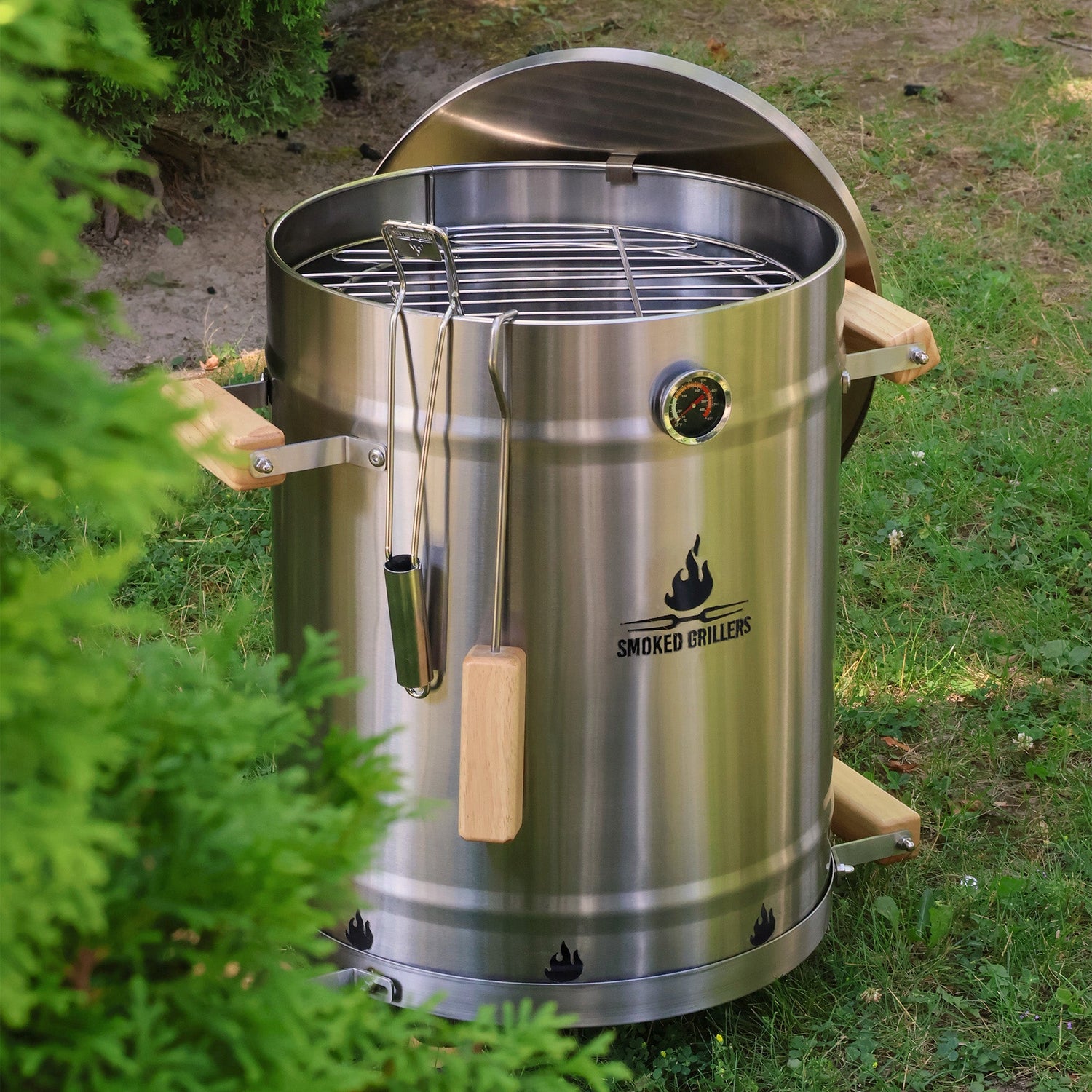 Stainless steel barbecue grill on grass with greenery around